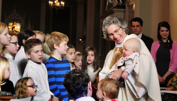 Lady pastor baptizing a baby with children looking on